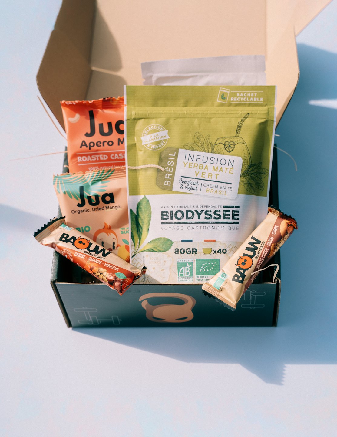 Open box overflowing with healthy organic snacks like nutrition bars and dried fruit.